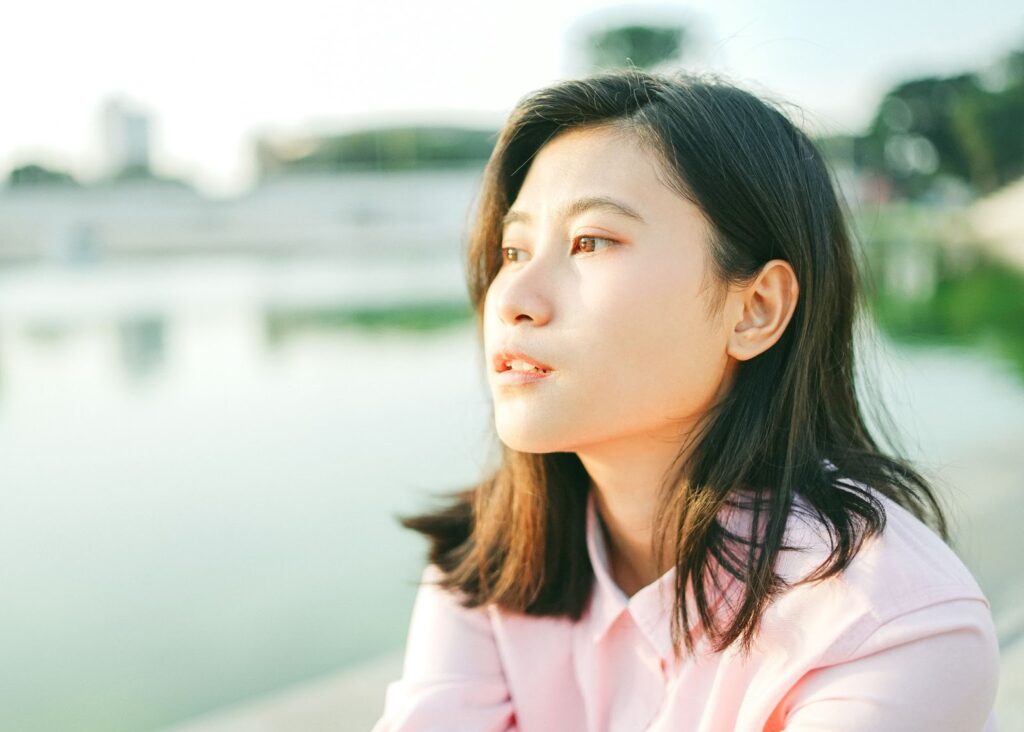 Asian woman in a pink shirt with dark hair pulled over her ear