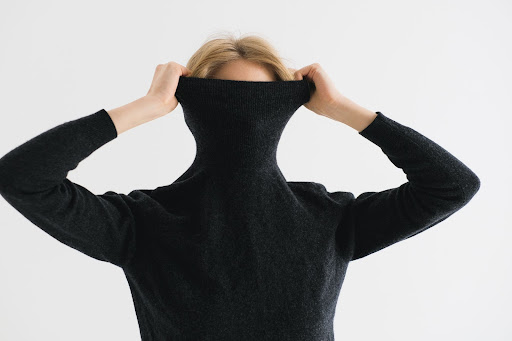 Blonde woman pulling up a turtleneck sweater to hide her face.